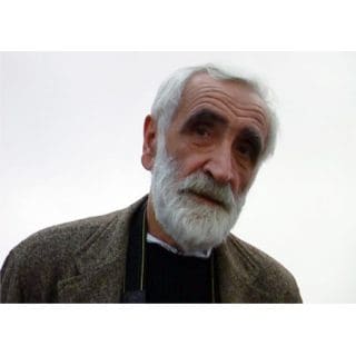 Elderly man with white beard, wearing jacket.