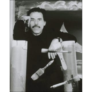 Man posing with paintbrushes and artwork.