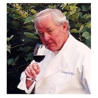Chef holding wine glass in garden setting.
