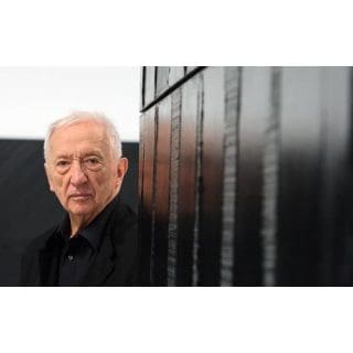 Older man standing beside a black wall.