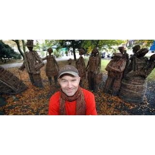 Man posing with whimsical outdoor sculptures.