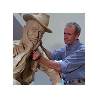 Man sculpting large clay statue with hat.